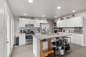 Large Side: Kitchen featuring white cabinets, an island with sink, appliances with stainless steel finishes, and under cabinet range hood