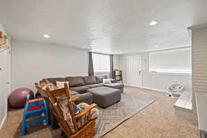 Large Side: Basement living room featuring baseboards, light colored carpet, a textured ceiling, a brick fireplace, and separate entrance