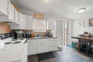 Smaller Side: Kitchen featuring dark countertops, electric range, white cabinets,  tile flooring, and sliding glass door.