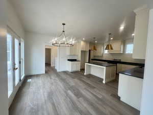 Kitchen with a chandelier, a kitchen island, baseboards, dark countertops, and wood finished floors