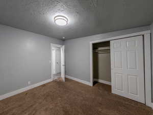 Unfurnished bedroom featuring a textured ceiling, carpet floors, a closet, and baseboards