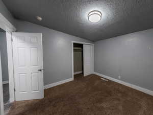 Unfurnished bedroom featuring carpet, lofted ceiling, a closet, a textured ceiling, and baseboards