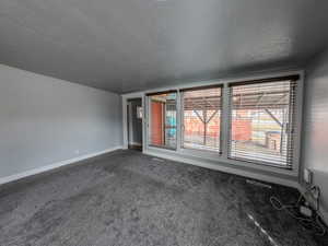 Carpeted empty room with a textured ceiling and baseboards