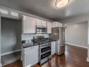 Kitchen with baseboards, tile counters, dark wood-style flooring, stainless steel appliances, and white cabinetry