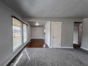 Spare room featuring a textured ceiling, dark colored carpet, visible vents, and baseboards