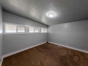 Empty room with lofted ceiling, a textured ceiling, carpet flooring, visible vents, and baseboards