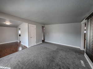 Unfurnished room featuring baseboards, visible vents, dark colored carpet, and a textured ceiling