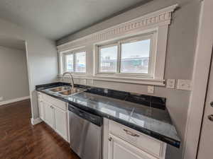 Kitchen with dark wood-style flooring, a sink, white cabinets, stainless steel dishwasher, and tile counters