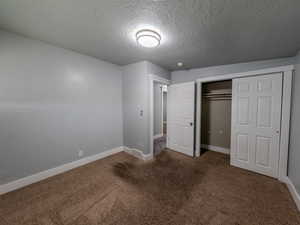 Unfurnished bedroom with a textured ceiling, dark colored carpet, a closet, and baseboards