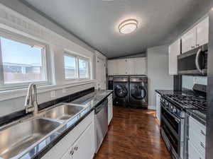 Kitchen featuring stainless steel appliances, dark countertops, white cabinetry, and independent washer and dryer