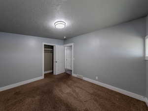 Unfurnished bedroom with a textured ceiling, carpet floors, visible vents, baseboards, and a closet