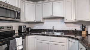 Kitchen with stainless steel appliances, decorative backsplash, white cabinets, a sink, and dark stone counters