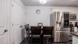 Kitchen featuring dark tile patterned floors, white cabinetry, appliances with stainless steel finishes, dark stone counters, and tasteful backsplash