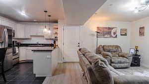 Kitchen with dark countertops, open floor plan, white cabinetry, pendant lighting, and a sink