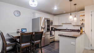 Kitchen featuring appliances with stainless steel finishes, a peninsula, white cabinetry, open shelves, and a sink