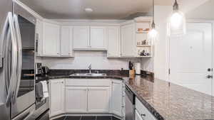 Kitchen with a sink, white cabinets, appliances with stainless steel finishes, open shelves, and pendant lighting