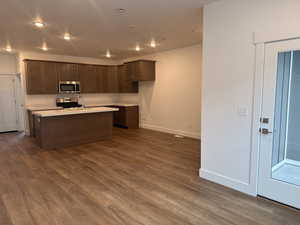 Kitchen with appliances with stainless steel finishes, dark brown cabinets, dark hardwood / wood-style floors, and a center island with sink