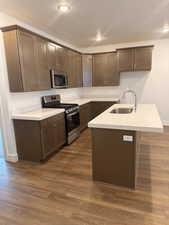 Kitchen featuring sink, stainless steel appliances, dark wood-type flooring, an island with sink, and dark brown cabinets