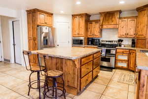 Kitchen with appliances with stainless steel finishes, brown cabinets, a center island, light countertops, and premium range hood