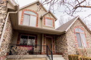 View of front of home featuring stone siding, a porch, and roof with shingles