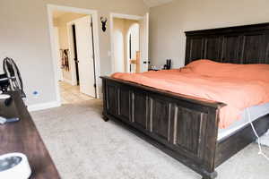 Bedroom featuring arched walkways, light colored carpet, baseboards, and light tile patterned floors