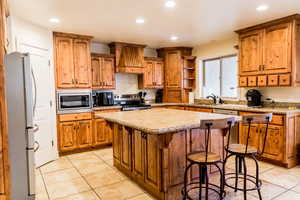 Kitchen with a center island, custom exhaust hood, stainless steel appliances, light countertops, and a kitchen breakfast bar