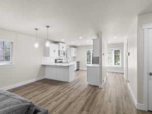 Kitchen with open floor plan, a peninsula, stainless steel appliances, light countertops, and white cabinetry