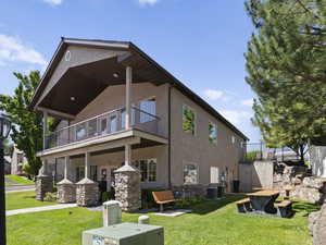 Rear view of property with a yard, a balcony, and stucco siding