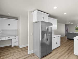 Kitchen with stainless steel fridge with ice dispenser, open floor plan, light countertops, white cabinetry, and built in desk