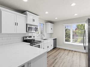 Kitchen with stainless steel appliances, white cabinets, a sink, and light stone counters