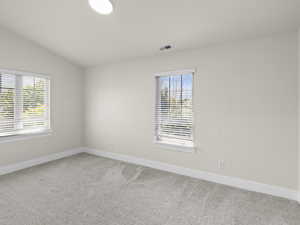 Carpeted empty room featuring visible vents, vaulted ceiling, and baseboards