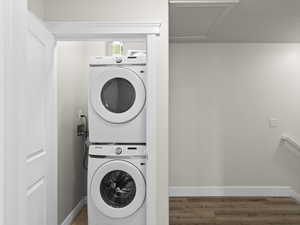 Clothes washing area featuring stacked washer / dryer, wood finished floors, and baseboards