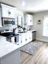 Kitchen featuring appliances with stainless steel finishes, light wood-style floors, white cabinets, and a sink