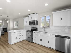 Kitchen with a peninsula, stainless steel appliances, light countertops, white cabinetry, and a sink