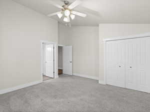 Unfurnished bedroom featuring a closet, a ceiling fan, light carpet, vaulted ceiling, and baseboards