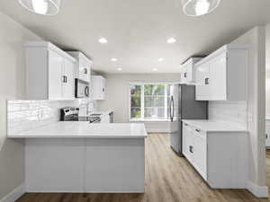 Kitchen featuring stainless steel appliances, white cabinets, light countertops, and a peninsula