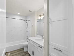 Bathroom featuring visible vents, toilet, shower / tub combination, wood finished floors, and vanity