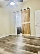 Unfurnished bedroom with a barn door, baseboards, ceiling fan, and wood finished floors