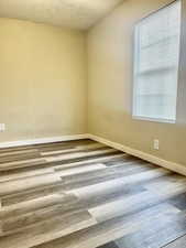 Spare room featuring a textured ceiling, baseboards, and wood finished floors