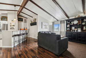 Living area with vaulted ceiling with beams, baseboards, and dark wood finished floors