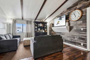 Living room with lofted ceiling with beams, wood walls, a textured ceiling, and wood finished floors