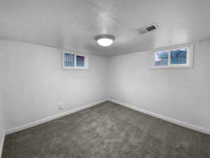 Basement with baseboards, visible vents, dark carpet, and a textured ceiling