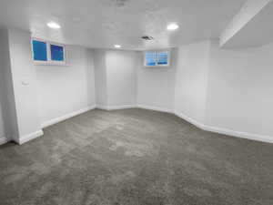 Below grade area featuring dark colored carpet, a textured ceiling, and baseboards