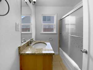 Bathroom with combined bath / shower with glass door, plenty of natural light, tile patterned flooring, and vanity