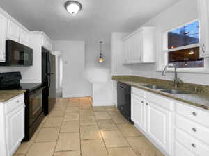 Kitchen with dark stone countertops, black appliances, white cabinetry, pendant lighting, and a sink