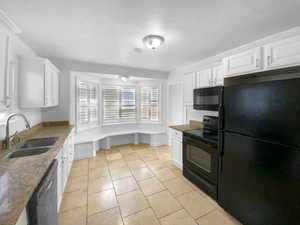 Kitchen featuring light tile patterned flooring, a sink, white cabinetry, dark stone counters, and black appliances