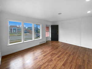 Unfurnished room featuring dark wood-style flooring, visible vents, and baseboards