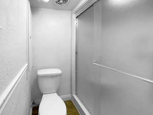 Full bathroom featuring a textured wall, toilet, visible vents, a shower stall, and tile patterned floors