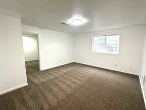 Empty room featuring baseboards, visible vents, dark carpet, and a textured ceiling