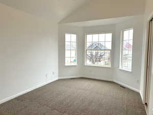 Carpeted empty room featuring visible vents, vaulted ceiling, and baseboards